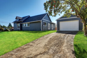 Gray house with a detached garage and a dirt driveway, surrounded by green grass and trees, illustrating a common residential property with separate structure, shich may be used for business purposes. | Huff Insurance Blog